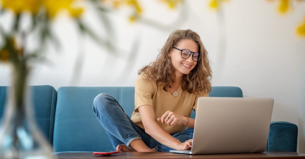 Kvinne som sitter i sofa og bruker PC